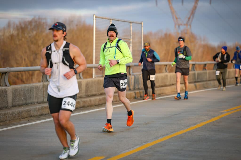 An older trail runner crossing the finish line smiling, showing travel at any age is possible